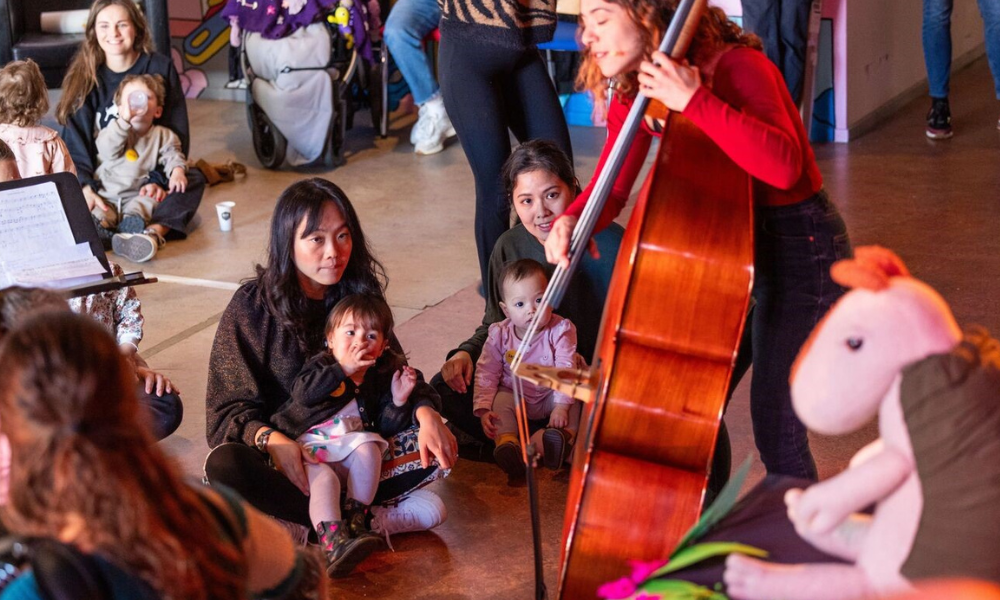 Kinderen en moeders kijken naar vrouw die een cello bespeelt