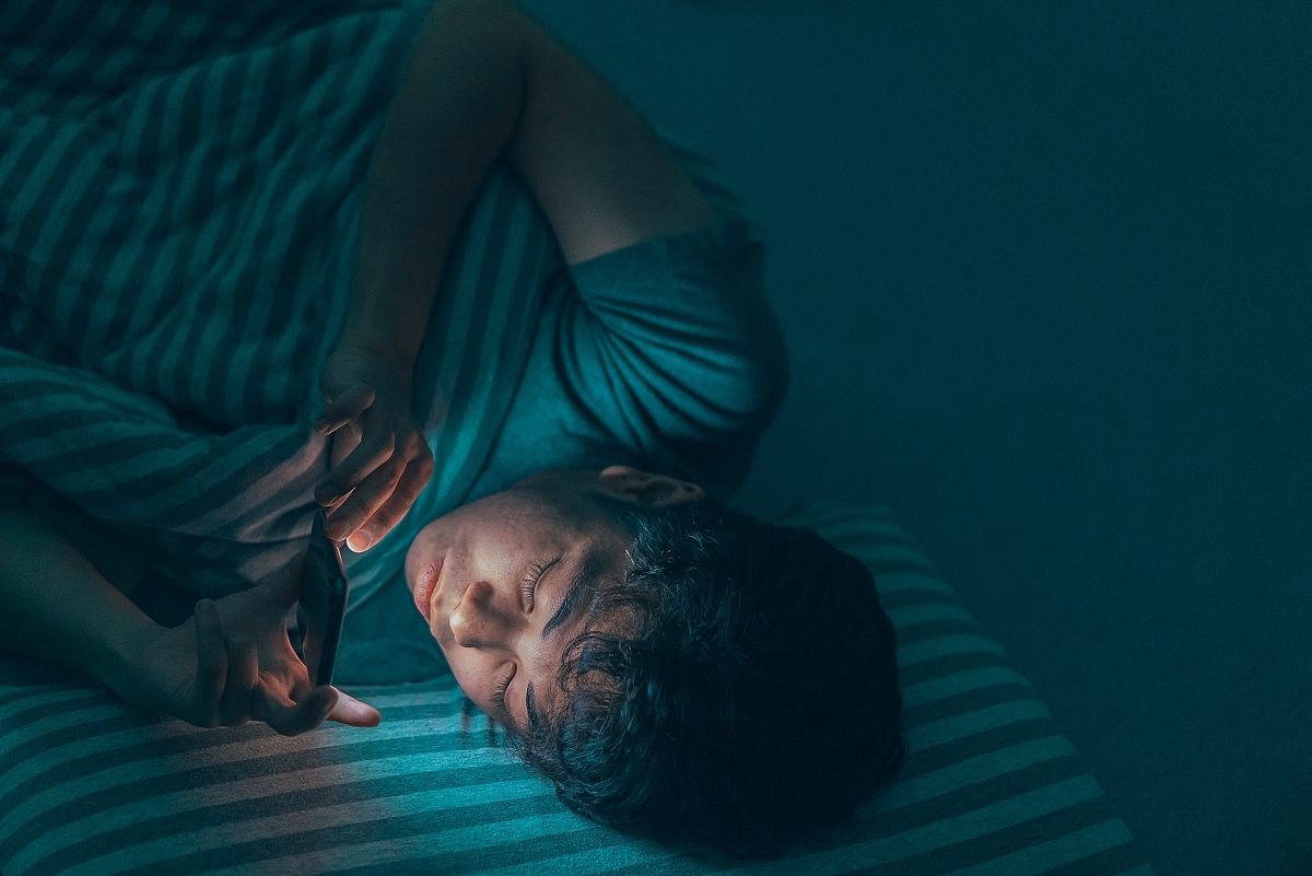 Jongen ligt in bed en kijkt op telefoon