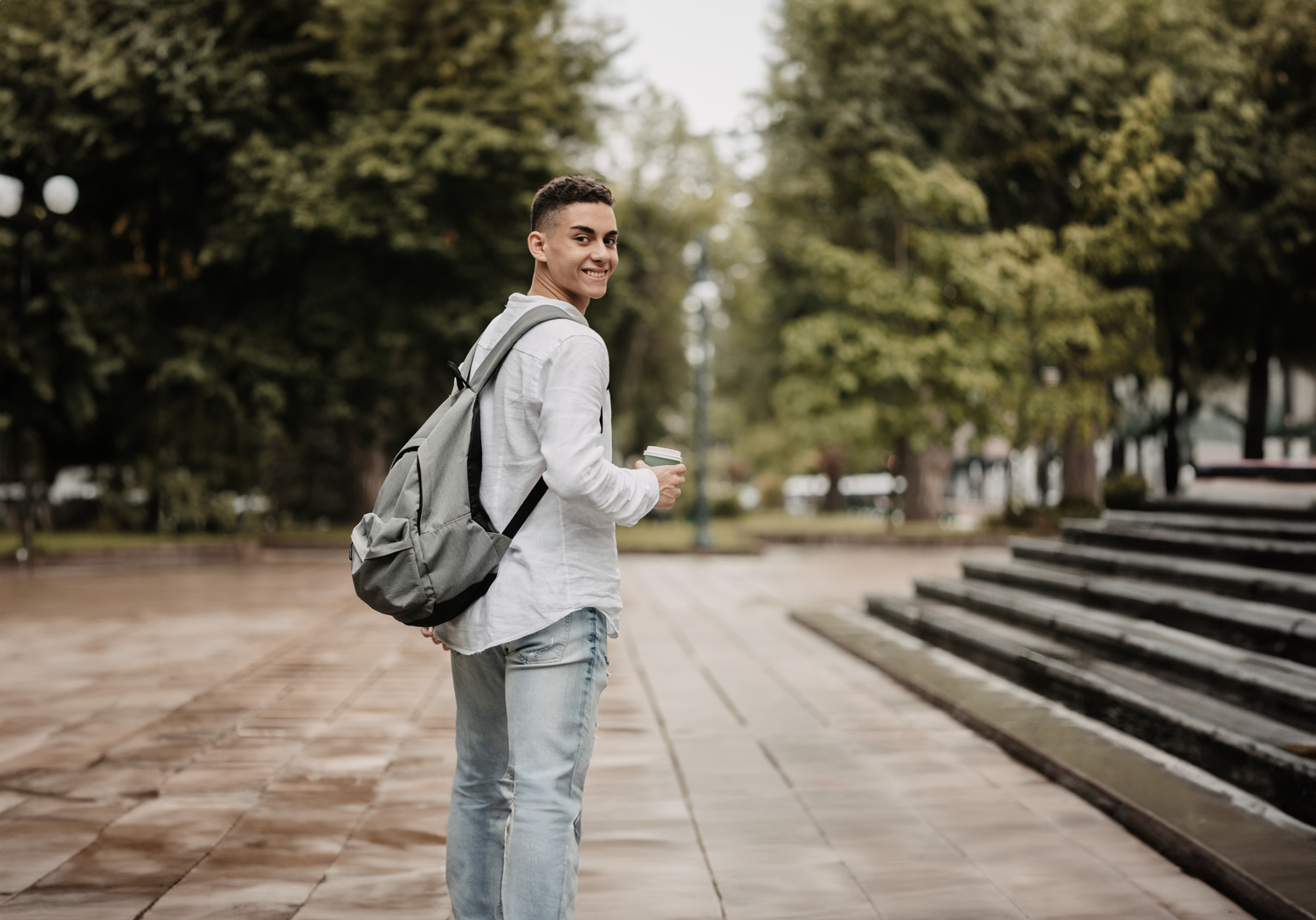 Jongen met rugzak en koffie kijkt om