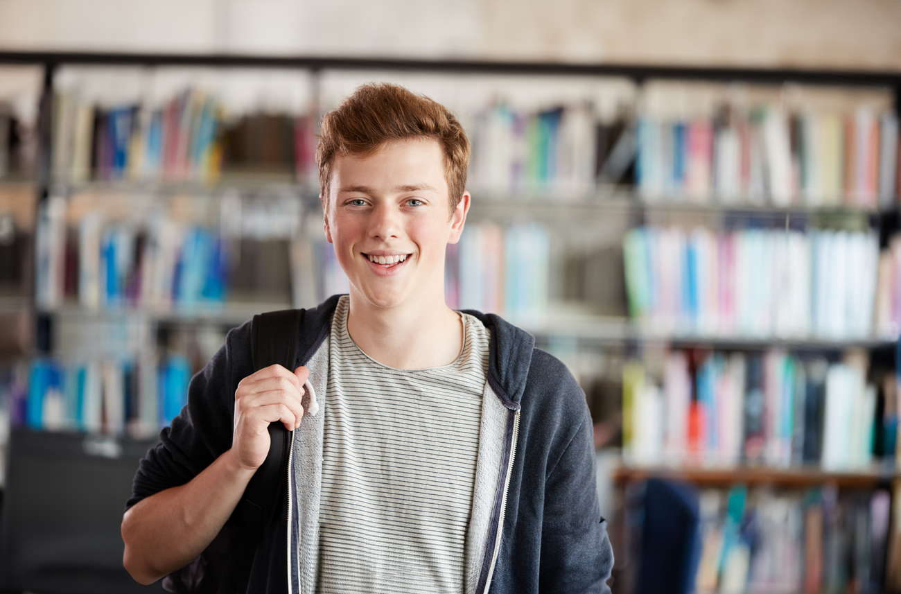 Jongen staat in bibliotheek en kijkt blij