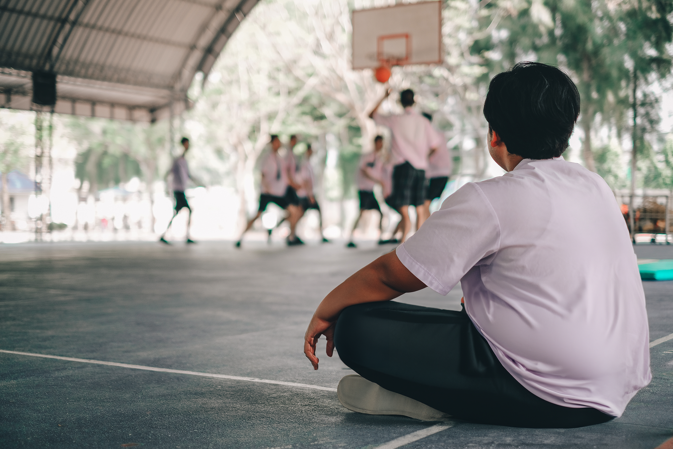 Jongen met overgewicht zit langs de kant van basketbalwedstrijd