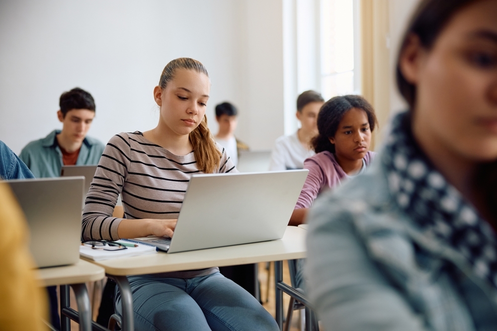 Tiener meisje zit achter laptop in klaslokaal met klasgenoten