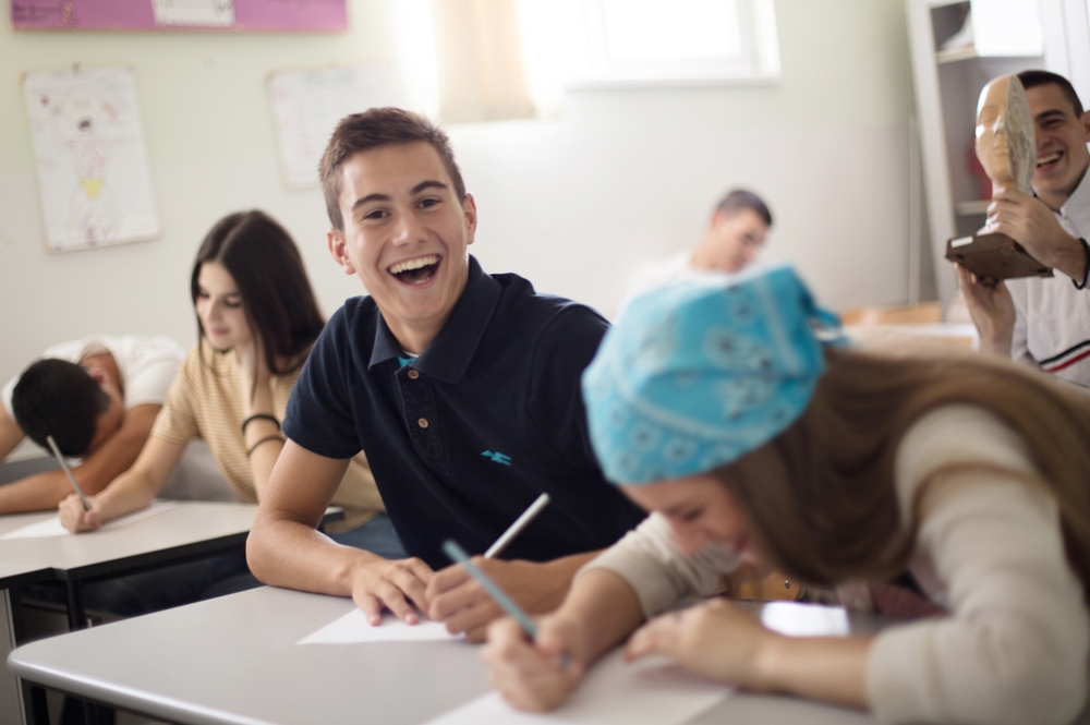 Tiener jongen zit lachend in de klas