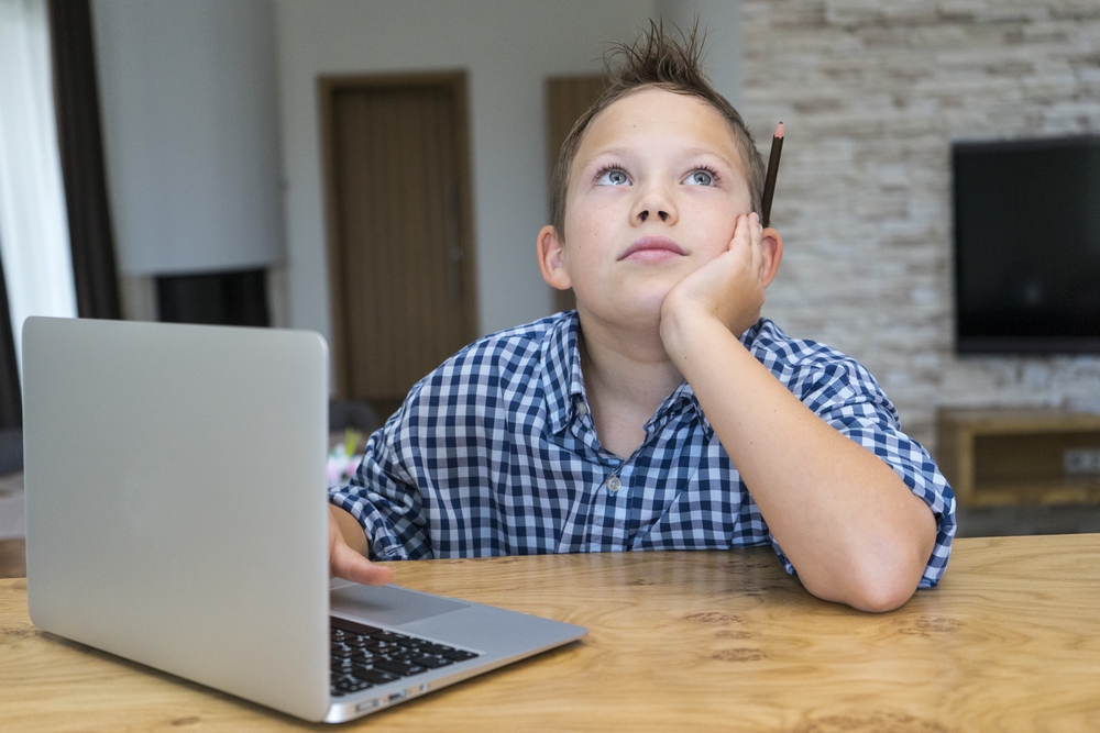 Jongen zit achter laptop maar kijkt afgeleid naar boven