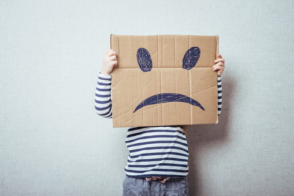 Kind die een kartonnen bord met een verdrietig gezicht voor zich houdt