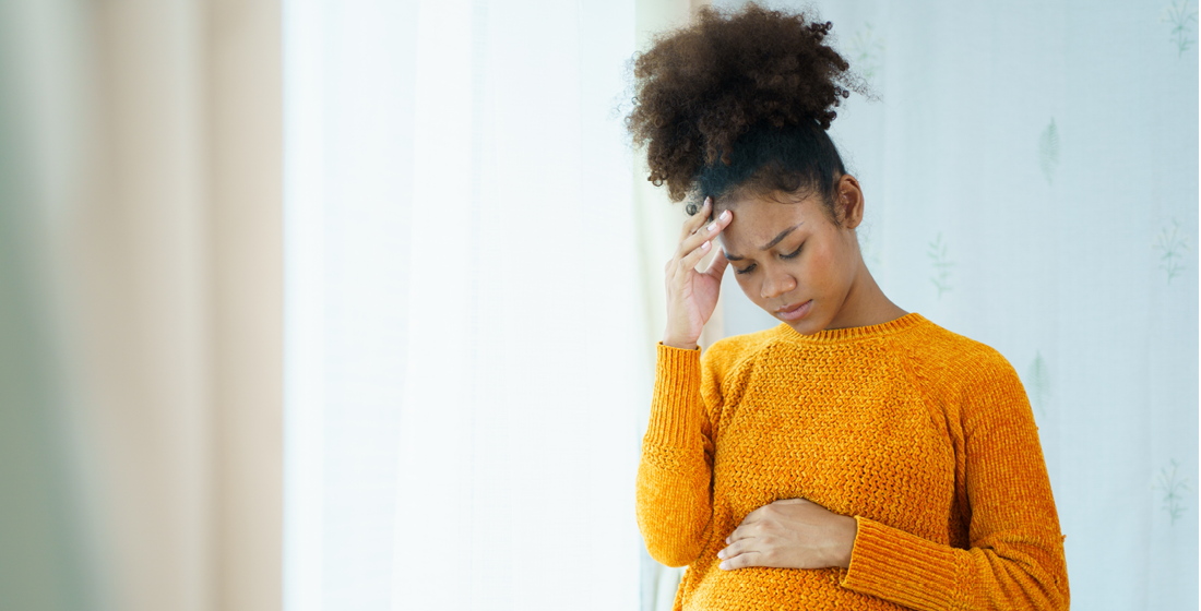 Zwangere die naar haar hoofd en buik grijpt
