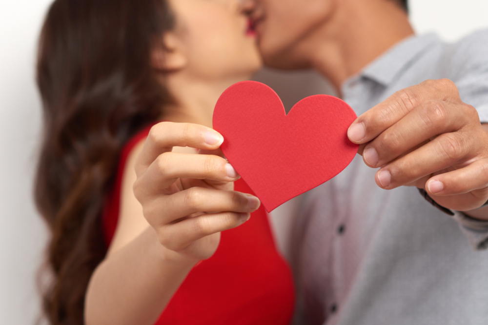 Twee jongeren kussen en houden een papieren hart vast