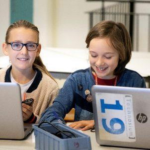 Twee jongeren zitten achter laptop in klaslokaal