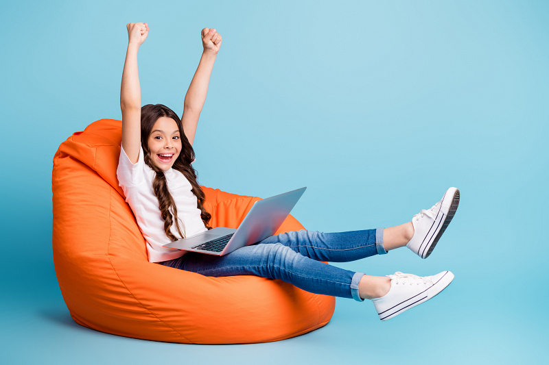 Kind met laptop zit op zitzak en juicht