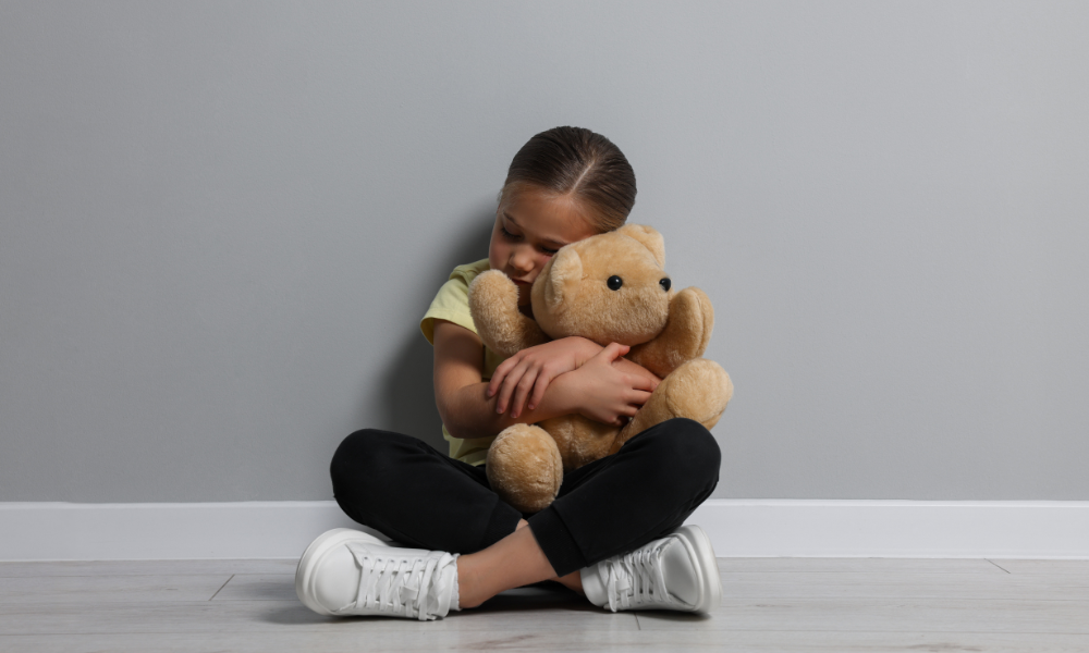 Meisje die op de grond zit en een knuffelbeer vasthoudt